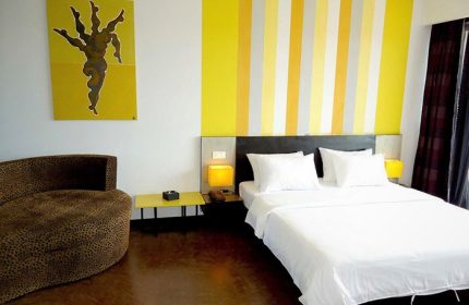 Gay-friendly hotel room at men's resort & spa. Features a bed, chair, yellow accents, and artwork. Modern design for gay travelers.