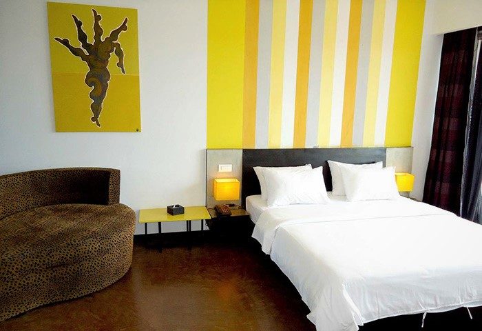 Gay-friendly hotel room at men's resort & spa. Features a bed, chair, yellow accents, and artwork. Modern design for gay travelers.