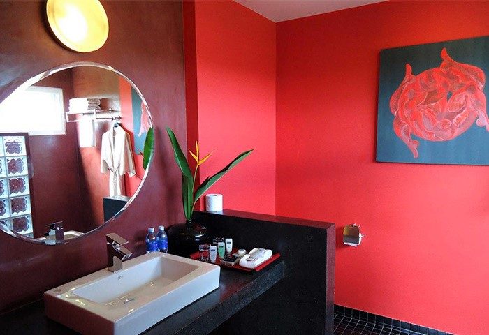Gay-friendly hotel men's resort spa bathroom with red walls, round mirror, and modern sink. Luxury gay hotel for men's travel.