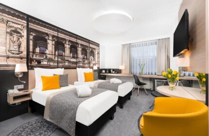 Mercure Budapest City Center Hotel room. Gay-friendly hotel with twin beds, yellow accents, desk, and city view wallpaper. Modern, comfortable stay.