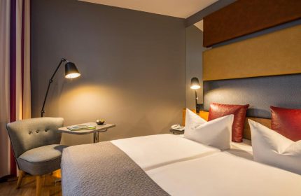 Gay-friendly Mercure Hotel Berlin Zentrum room. Modern design, double bed, chair, and reading lights. Comfortable stay in Berlin.