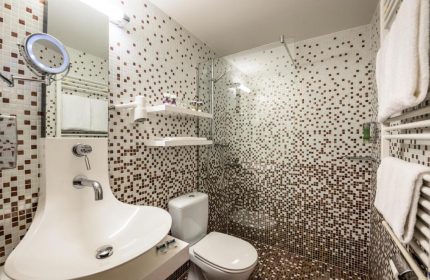 Bathroom at Gay-Friendly Mercure Hotel Berlin Zentrum. Shower, toilet, and unique sink design. Mosaic tile decor. Ideal gay travel accommodation.