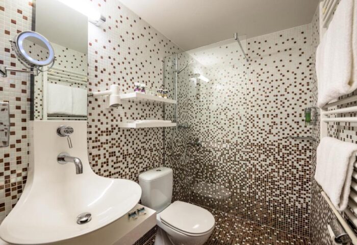 Bathroom at Gay-Friendly Mercure Hotel Berlin Zentrum. Shower, toilet, and unique sink design. Mosaic tile decor. Ideal gay travel accommodation.