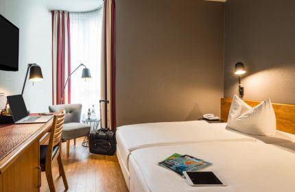Mercure Hotel Berlin Zentrum guest room. Gay-friendly hotel with twin beds, desk, chair, and luggage. Ideal for gay travelers in Berlin.