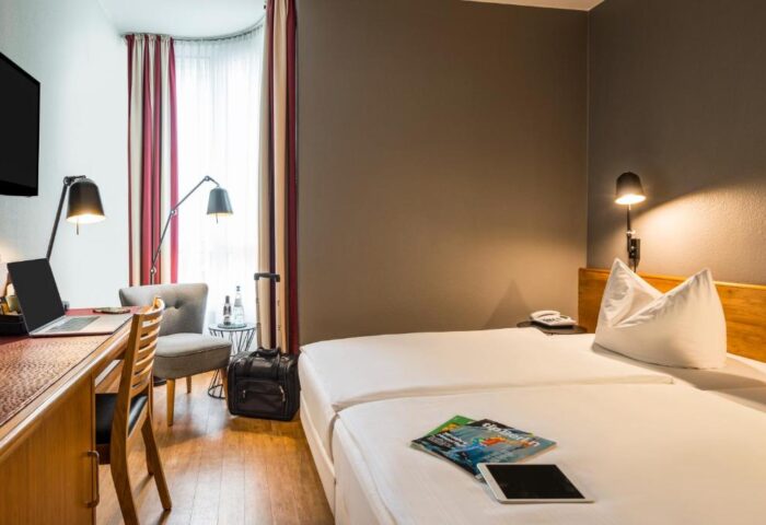 Mercure Hotel Berlin Zentrum guest room. Gay-friendly hotel with twin beds, desk, chair, and luggage. Ideal for gay travelers in Berlin.