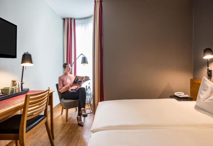Gay-Friendly Mercure Hotel Berlin Zentrum room. Woman reading. Desk, chair, bed, and lamps. Modern decor. Gay travel lodging.