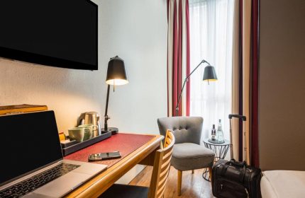 Mercure Hotel Berlin Zentrum room: desk with laptop, chair, & luggage. Gay-friendly hotel for gay men travelers in Berlin. Modern, comfortable.