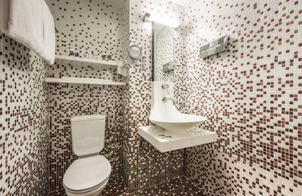 Bathroom at Mercure Hotel Berlin Zentrum, a gay-friendly hotel. Features mosaic tiles, toilet, modern sink, and shelves. #gaytravel
