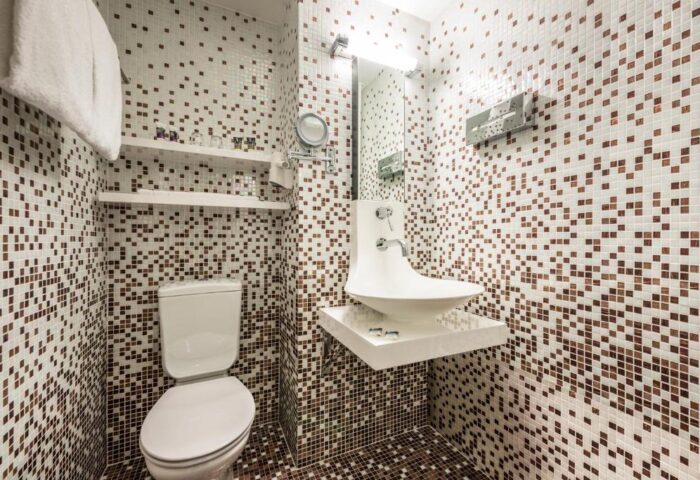 Bathroom at Mercure Hotel Berlin Zentrum, a gay-friendly hotel. Features mosaic tiles, toilet, modern sink, and shelves. #gaytravel