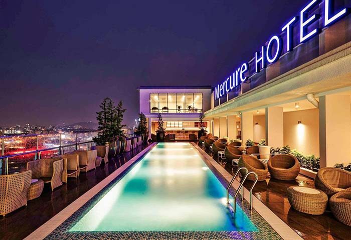 Mercure Kuala Lumpur Shaw Parade gay-friendly hotel rooftop pool at night. City view, bar, and lounge chairs. Perfect for gay travel.