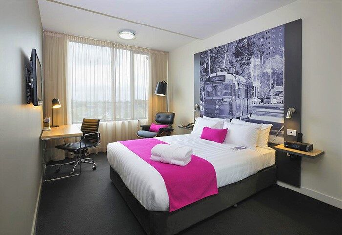 Mercure Melbourne Therry Street gay-friendly hotel room. Bed with pink accents, desk, and tram mural. Modern, comfortable lodging.