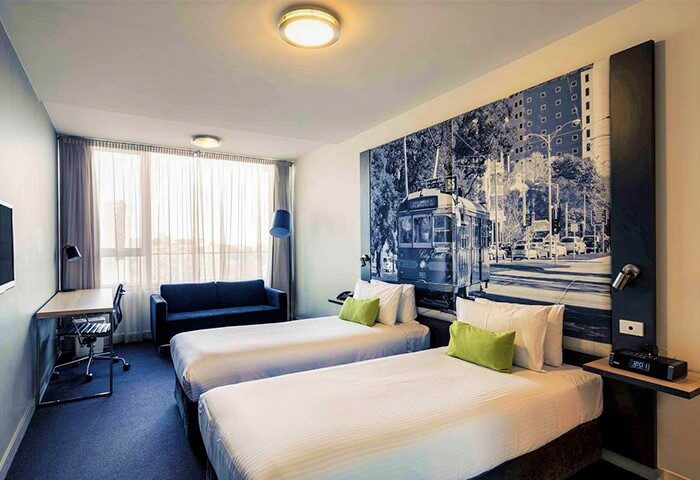 Mercure Melbourne Therry Street hotel room with twin beds, desk, and sofa. Gay-friendly hotel with tram mural. Melbourne travel for gay men.