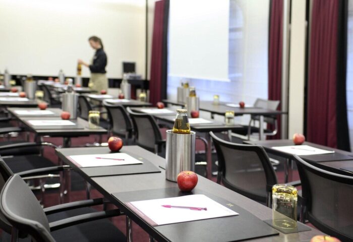 Mercure Munich City Center Hotel conference room setup. Tables with papers, pens, apples, drinks. Gay-friendly hotel for events.