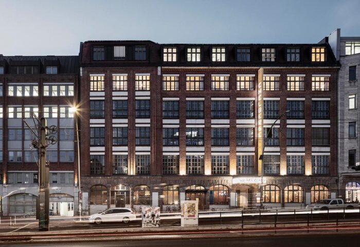 Michelberger Hotel facade at dusk. Gay-friendly hotel in Berlin, Germany. Brick building with illuminated windows. Travel advice for gay men.