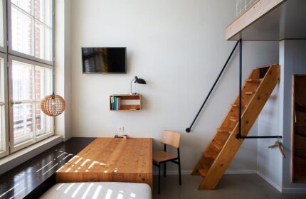 Michelberger Hotel room: Wooden stairs to loft, bed, table, chair, TV, lamp, and large window. Gay-friendly hotel for gay travelers.