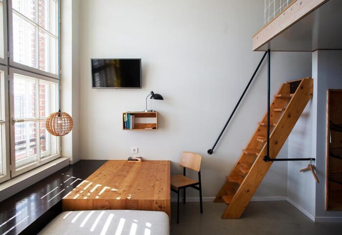 Michelberger Hotel room: Wooden stairs to loft, bed, table, chair, TV, lamp, and large window. Gay-friendly hotel for gay travelers.