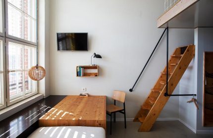 Michelberger Hotel room: Wooden stairs to loft, bed, table, chair, TV, lamp, and large window. Gay-friendly hotel for gay travelers.
