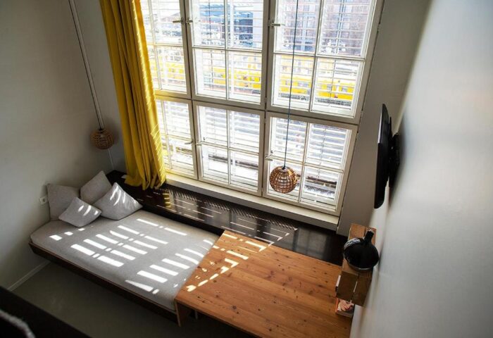 Michelberger Hotel room interior, a gay-friendly hotel. Features a large window, bed, table, and modern decor. Great for gay men travel advice.