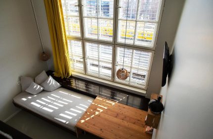 Michelberger Hotel room interior, a gay-friendly hotel. Features a large window, bed, table, and modern decor. Great for gay men travel advice.