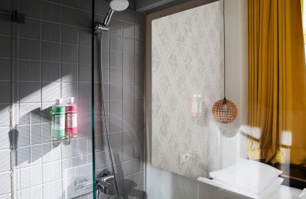 Michelberger Hotel bathroom. Shower with gray tiles and bottles, patterned wallpaper, and a round lamp. Gay-friendly hotel for gay travelers.