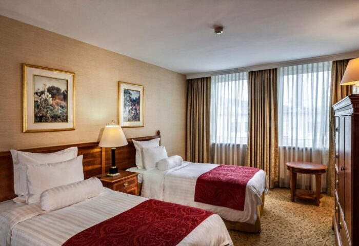 Millennium Court Budapest Marriott Executive Apartments room. Gay-friendly hotel with twin beds, red accents, and warm lighting. Comfy stay in Budapest.