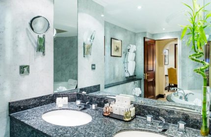 Bathroom view at the gay-friendly Millennium Gloucester Hotel London. Double sinks, marble counters, & bath products. Hotel room interior.