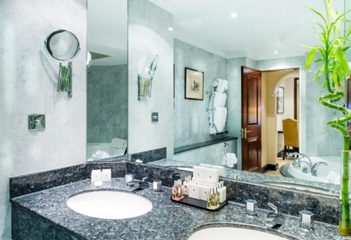 Bathroom view at the gay-friendly Millennium Gloucester Hotel London. Double sinks, marble counters, & bath products. Hotel room interior.