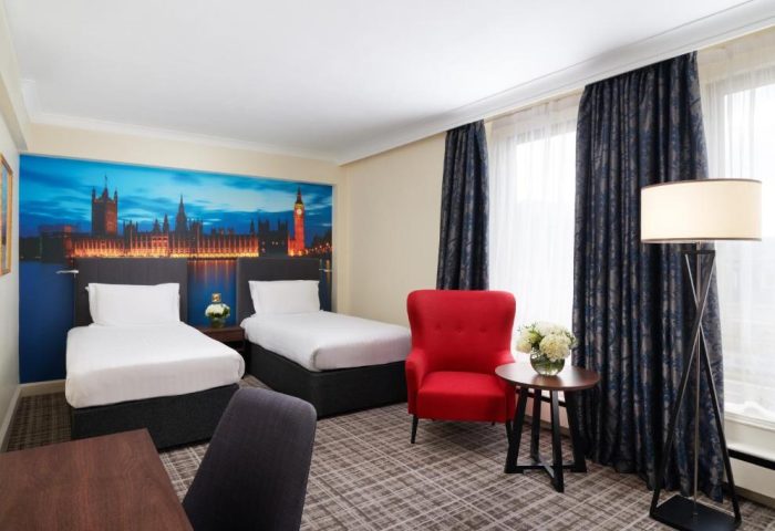 Millennium Gloucester Hotel London room with twin beds, red chair, and London skyline mural. Gay-friendly hotel for gay men travelers.