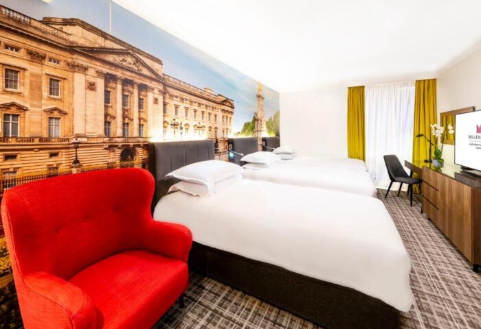 Millennium Gloucester Hotel London room. Gay-friendly hotel with twin beds, red chair, and Buckingham Palace mural. Ideal for gay travel.