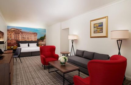 Millennium Gloucester Hotel London room. Gay-friendly hotel with red chairs, a grey sofa, and a bed with a Buckingham Palace mural.