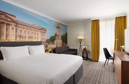 Millennium Gloucester Hotel London: Gay-friendly hotel room with a double bed, desk, sofa, and a mural of Buckingham Palace.