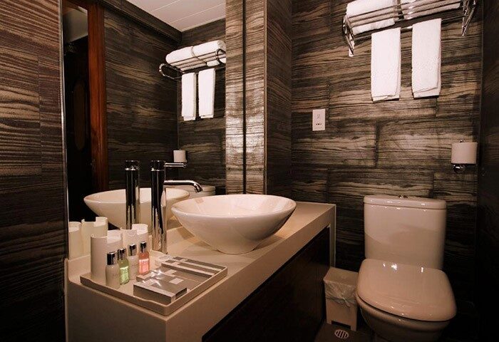 Mingle At The Eden gay-friendly hotel bathroom. White sink, toilet, and towels against a dark, wood-patterned wall. Modern design.