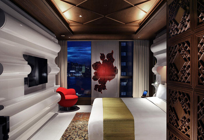 Mira Moon Hotel room. Gay-friendly hotel with a view of the city at night. Red chair, modern decor, and a comfortable bed. Luxury travel.