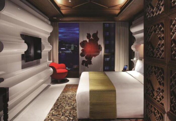 Mira Moon Hotel room, a gay-friendly hotel. Modern design with a red chair, white bed, and city view. Ideal for gay travel in Hong Kong.