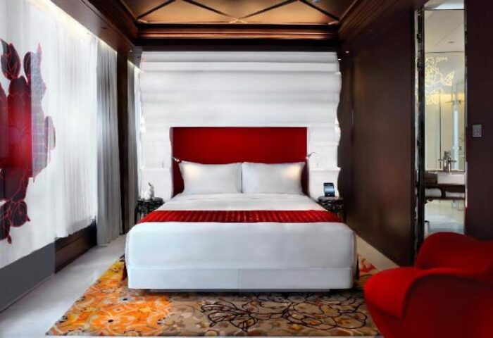 Mira Moon Hotel bedroom. Gay-friendly hotel with red accents, white linens, and a modern design. Bathroom visible in the background.