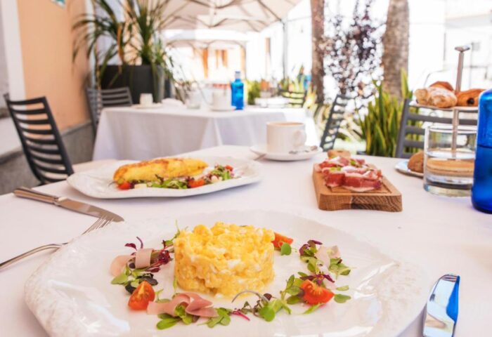 Breakfast at Gay-Friendly Hotel Mirador de Dalt Vila-Relais & Chateaux. Scrambled eggs, omelet, ham, and pastries on a white tablecloth.