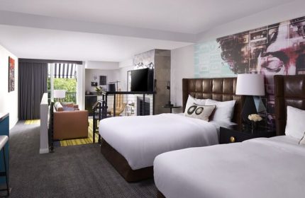 Montrose at Beverly Hills gay-friendly hotel room. Two beds with leather headboards, lounge area, balcony, and modern decor. Upscale travel.