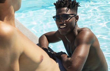 Two men at Montrose at Beverly Hills gay-friendly hotel pool. One in the water, smiling, wearing sunglasses. Gay travel, vacation.