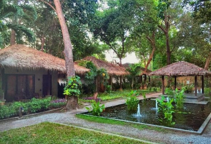 Mooban Talay Resort, a gay-friendly hotel. Thatched-roof bungalows, lush greenery, and a serene pond with fountains create a tranquil retreat.