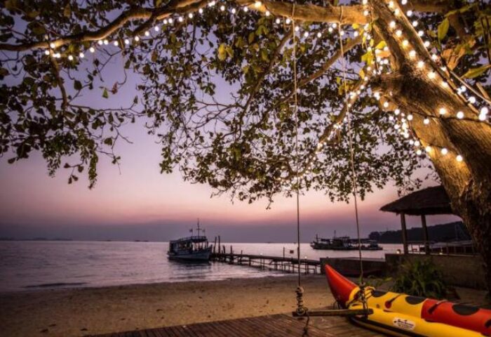 Sunset at Mooban Talay Resort, a gay-friendly hotel. Beach view with lights, boat, and swing. Perfect for gay men travel.