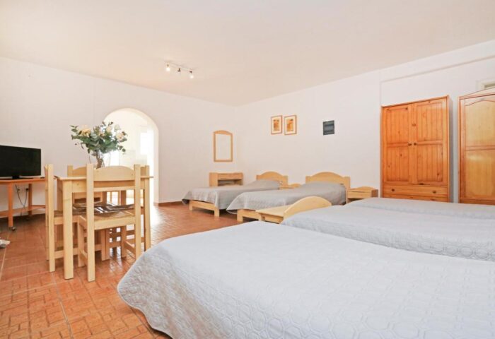 Morfoula's Studios: Interior of a gay-friendly hotel room featuring multiple beds, a dining table, and essential furniture. Comfortable stay.