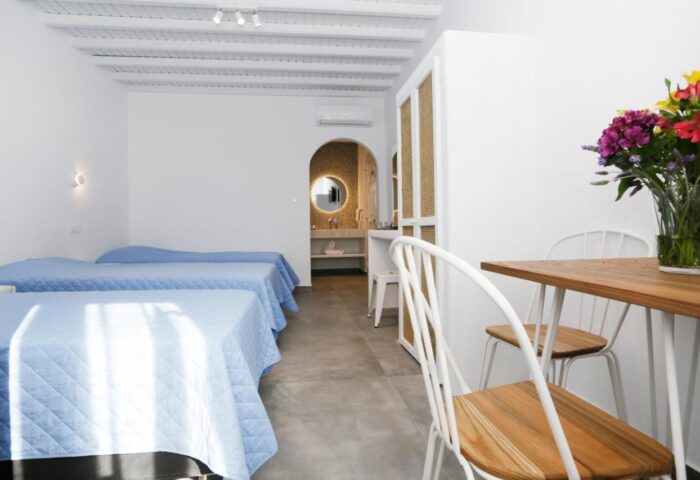 Morfoula's Studios room interior. Gay-friendly hotel with beds, table, chairs, and bathroom. Ideal for gay men's travel to Greece.