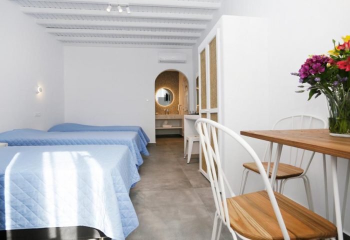 Morfoula's Studios room interior. Gay-friendly hotel with beds, table, chairs, and bathroom. Ideal for gay men's travel to Greece.