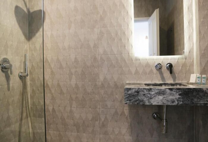 Morfoula's Studios gay-friendly hotel bathroom. Walk-in shower with glass partition, marble sink, and illuminated mirror. Modern design.
