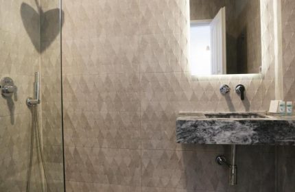 Morfoula's Studios gay-friendly hotel bathroom. Walk-in shower with glass partition, marble sink, and illuminated mirror. Modern design.