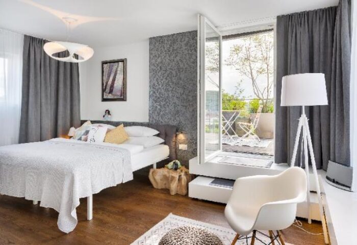 Mosaic House Design Hotel bedroom with balcony. Gay-friendly hotel room featuring a bed, chair, and outdoor space. Modern interior design.