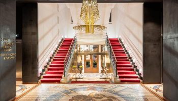 Grand entrance of Mosaic House Design Hotel, a gay-friendly hotel. Red carpeted stairs, mosaic floor, and modern chandelier.