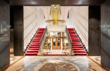 Grand entrance of Mosaic House Design Hotel, a gay-friendly hotel. Red carpeted stairs, mosaic floor, and modern chandelier.