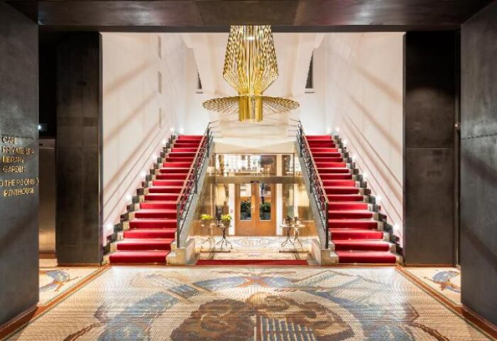 Grand entrance of Mosaic House Design Hotel, a gay-friendly hotel. Red carpeted stairs, mosaic floor, and modern chandelier.