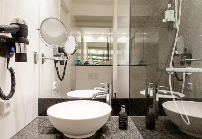 Motel One Koln-Neumarkt bathroom. Modern design with dual sinks, mirrors, hairdryer, and shower. Gay-friendly hotel in Cologne, Germany.